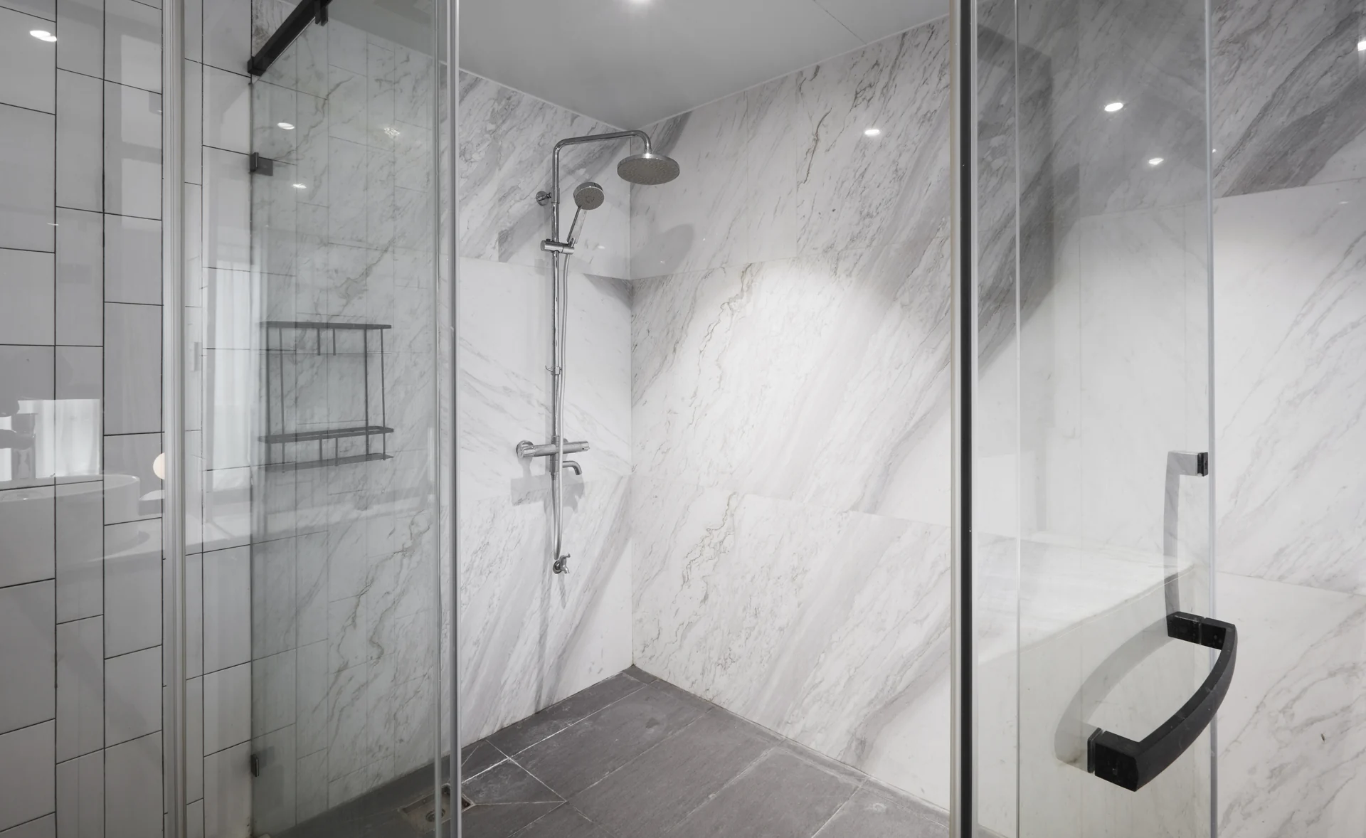 A glass shower enclosure with pale veined walls and dark hardware.