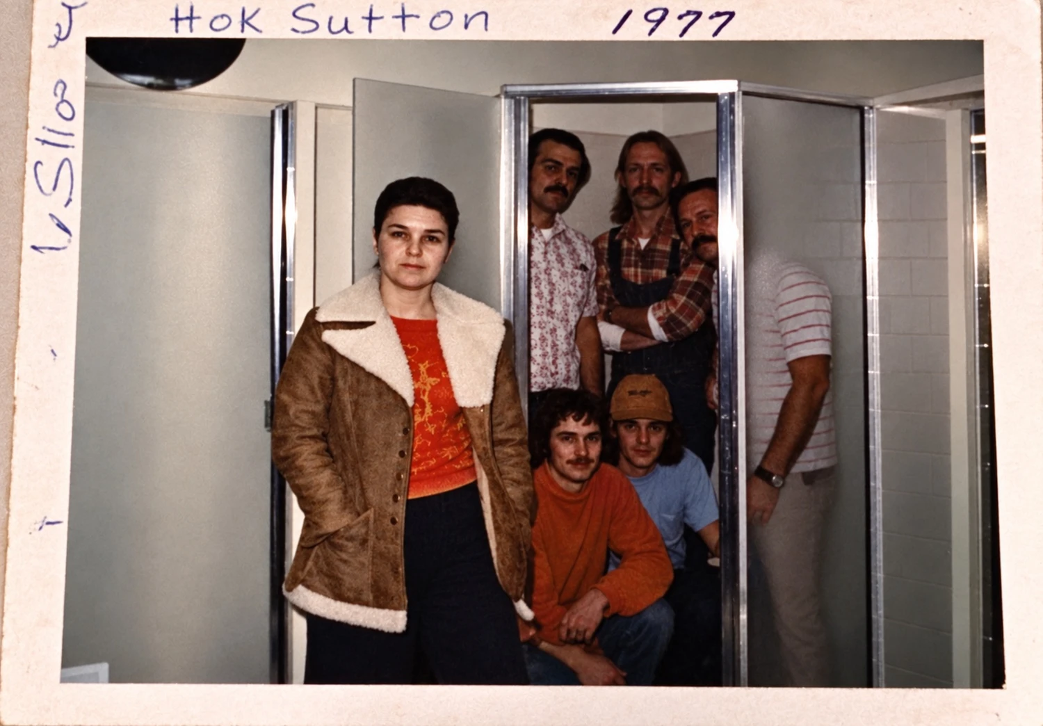 An archival group photograph inside a shower display, with a handwritten 1977 date along the original print border.