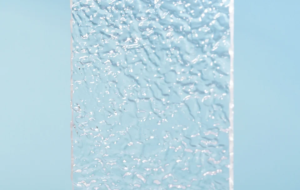 Close-up of an irregular textured glass surface against pale blue.
