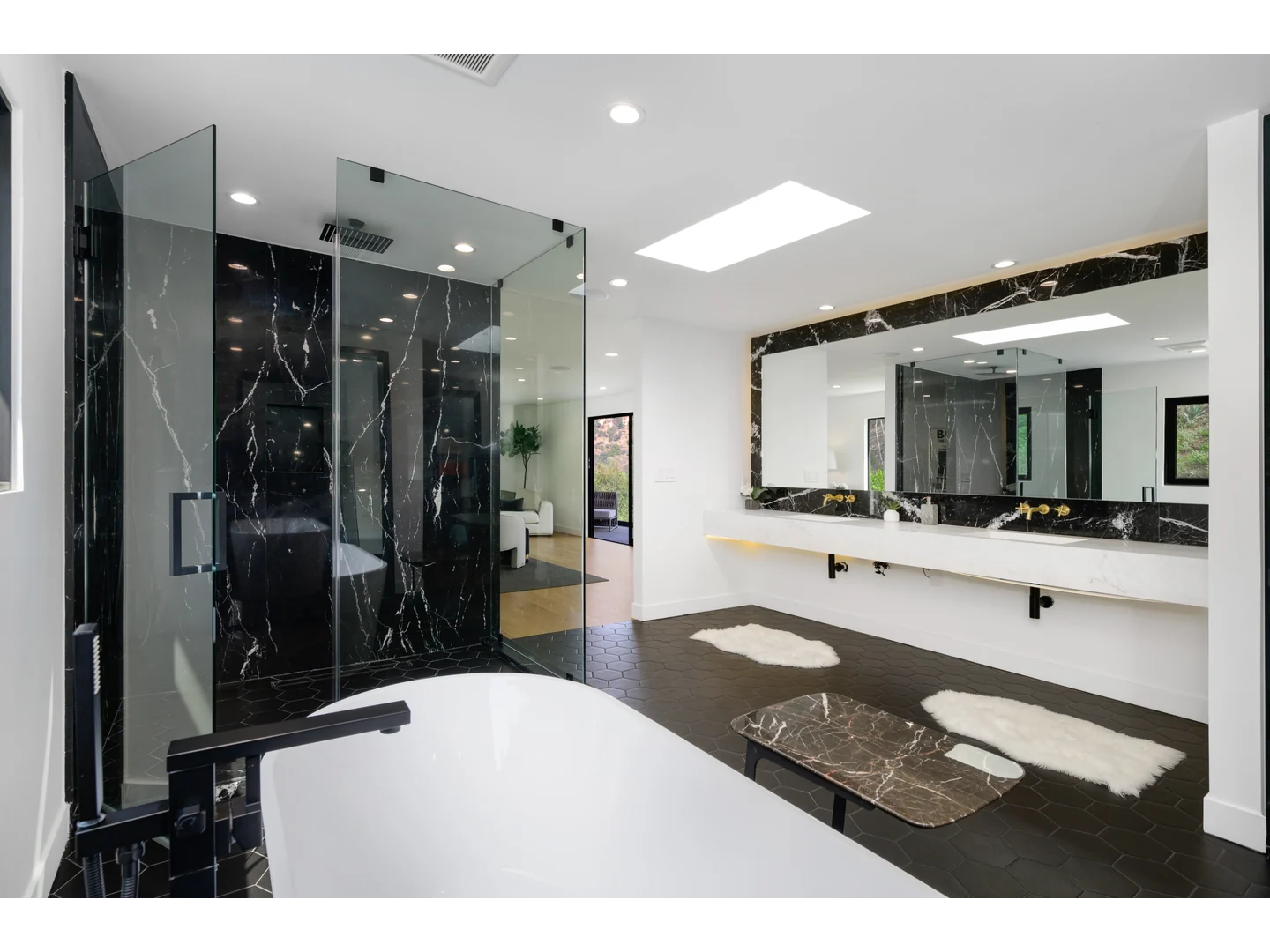 Clear glass shower enclosure against dark veined stone beside a freestanding bathtub.