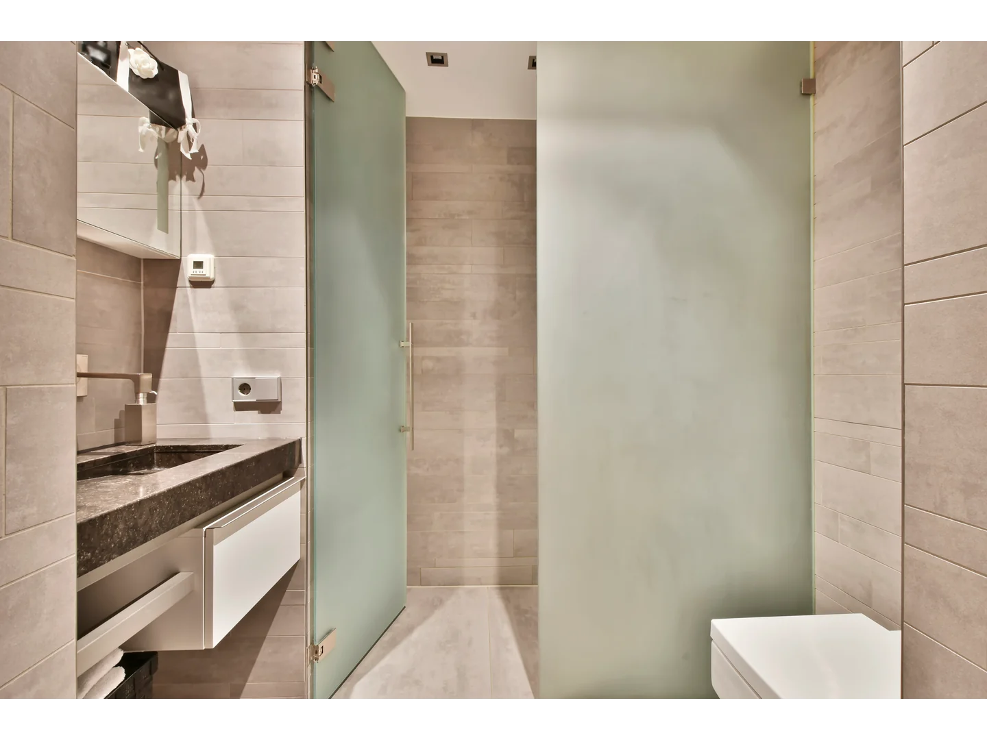 Open frosted-glass shower door beside a frosted partition and pale tiled walls.