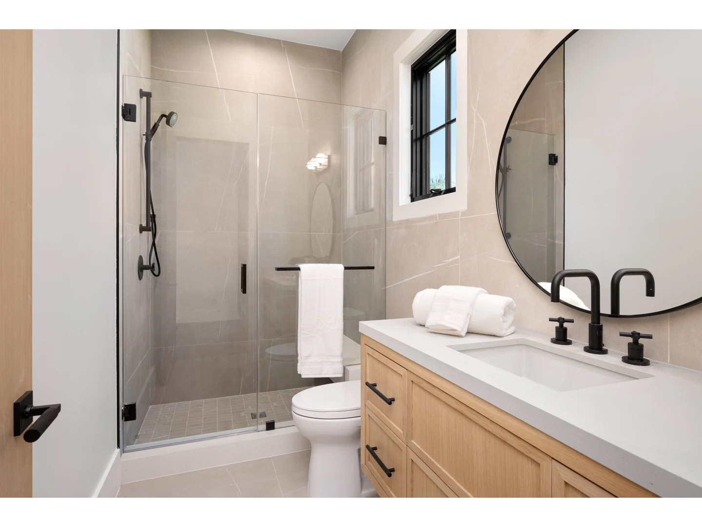 Clear inline shower door with black wall hinges and a compact vertical pull beside a wood vanity.