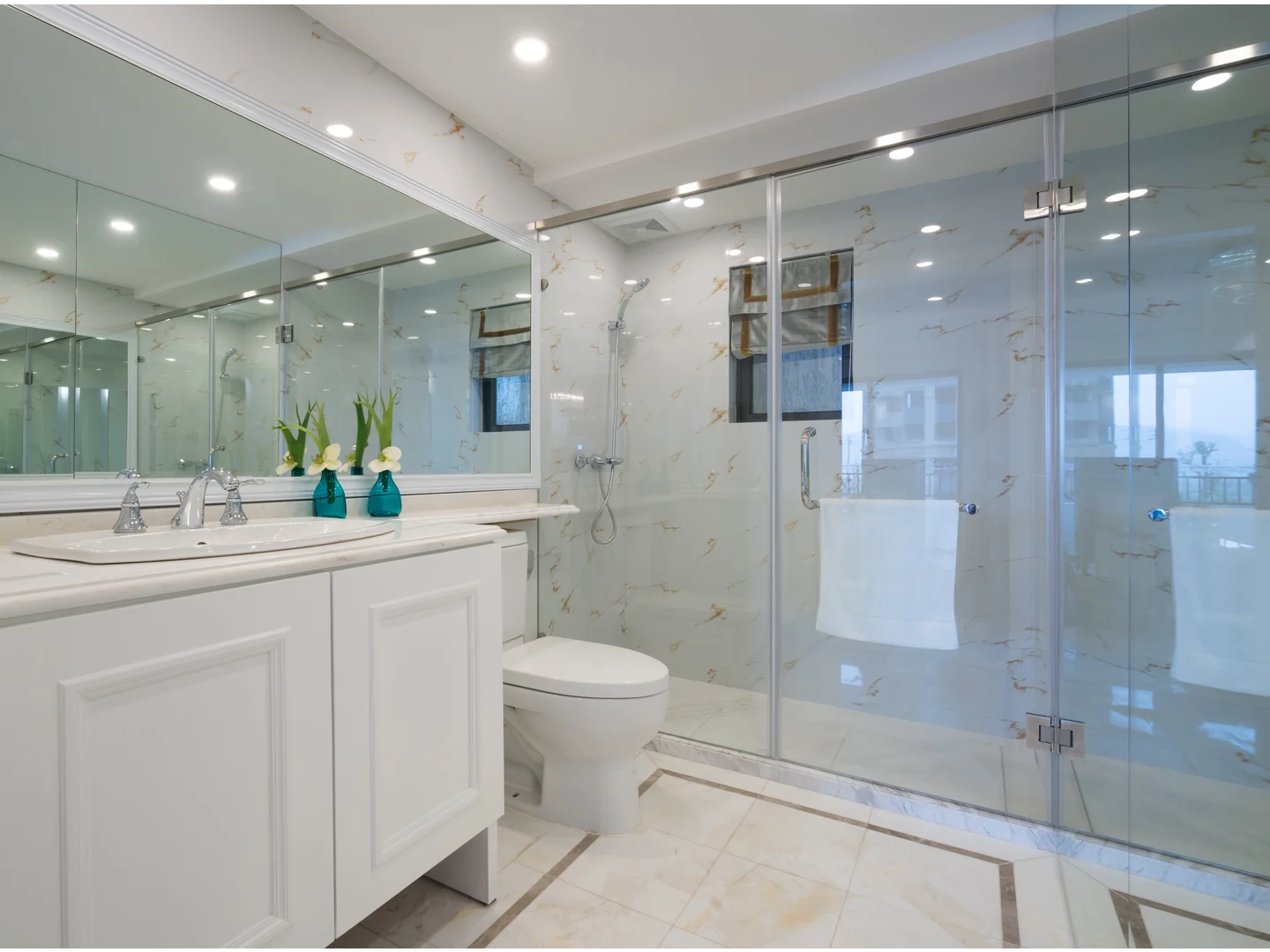 Wide clear-glass shower enclosure with silver-colored profiles beside a double vanity.