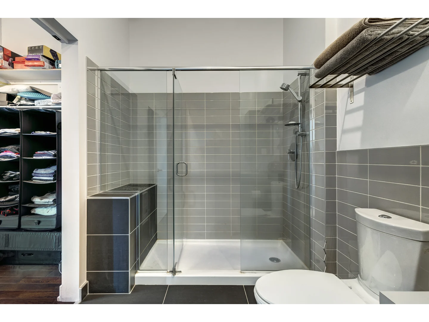 Clear shower door with a rounded polished pull, upper metal profile and a fixed panel above a tiled half wall.