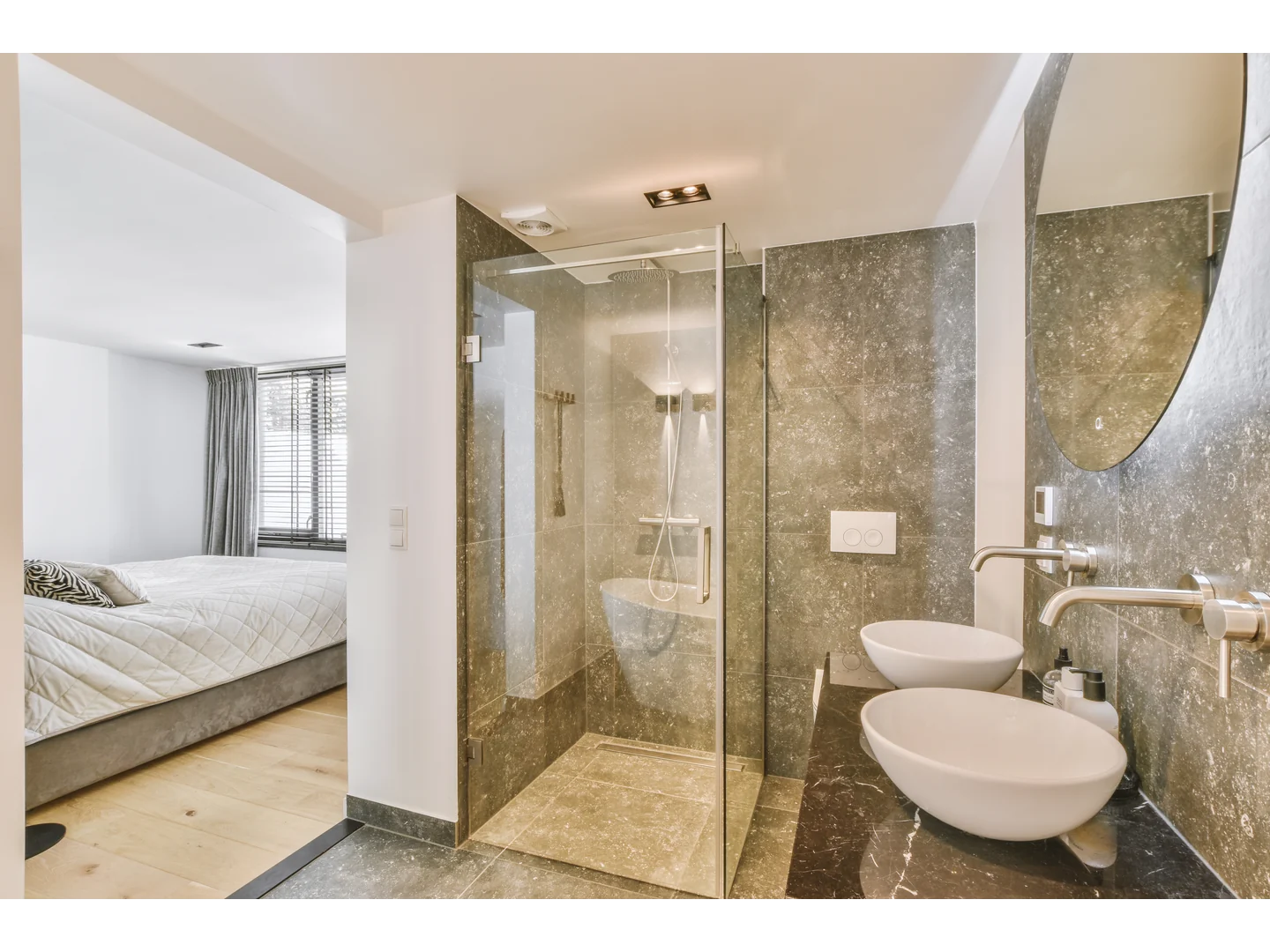 Clear corner shower enclosure with polished profiles beside dark stone walls and a white basin.