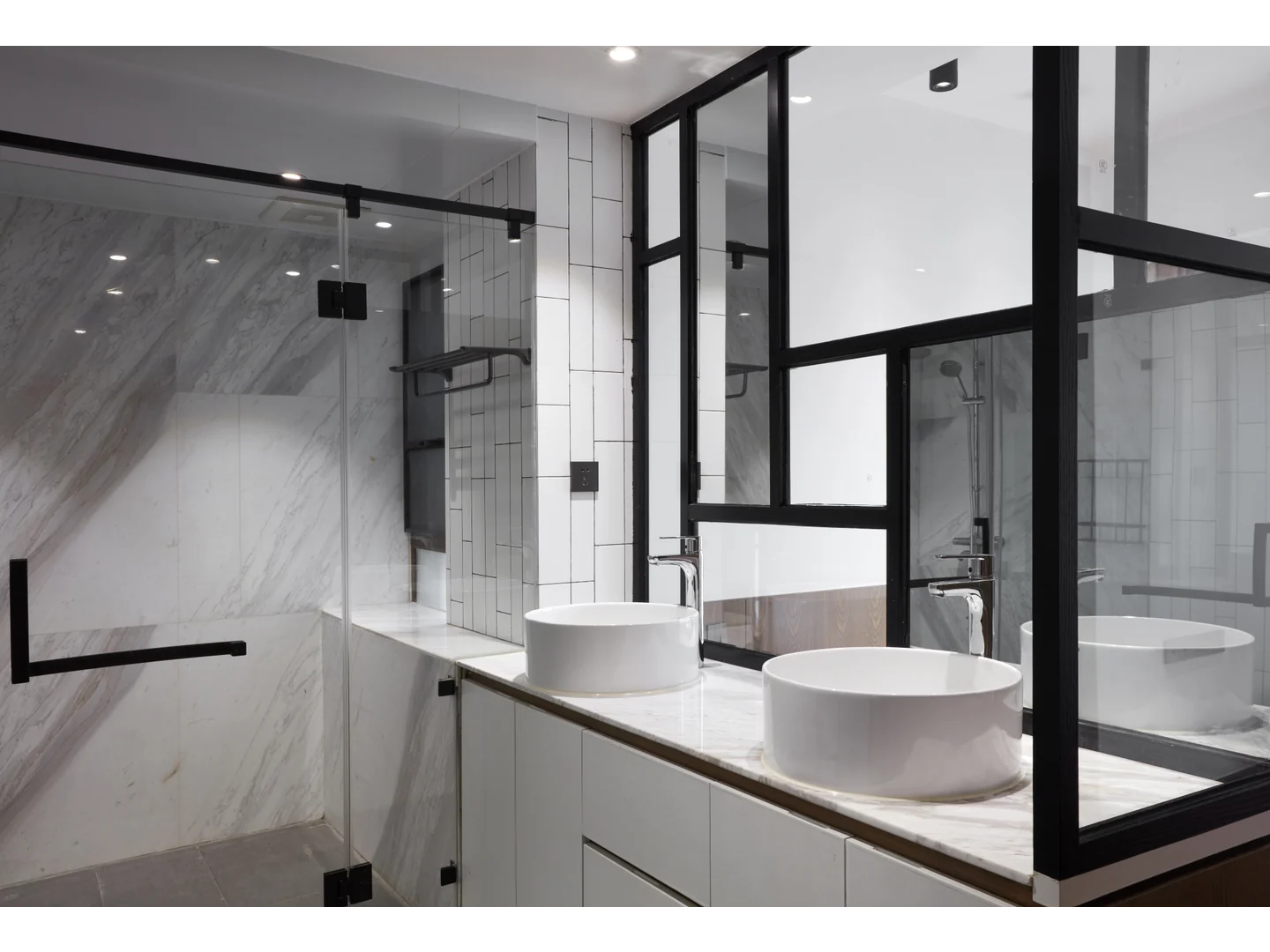 Clear shower enclosure with black fittings and an upper support beside two white basins.