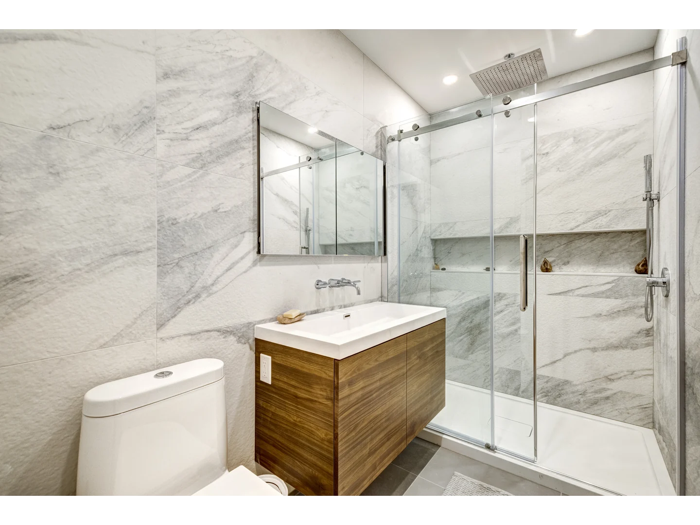 Clear inline sliding shower door with a polished metal top rail and a vertical pull beside a wood vanity.